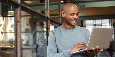 African American Man looking at results on laptop joyfully 